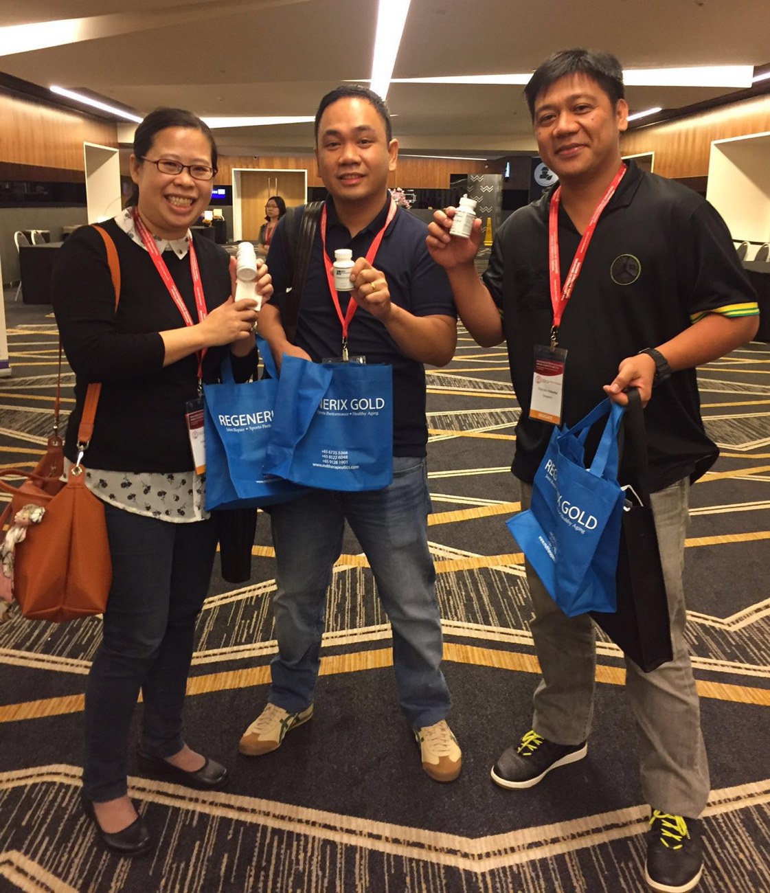 Three event attendees holding Regenerix Gold bottles and branded bags