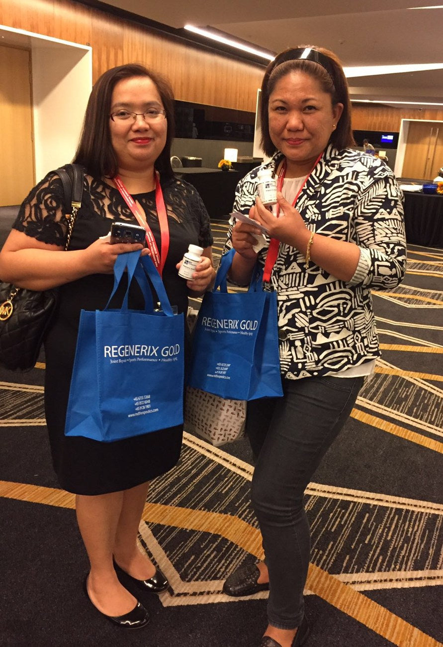 Two event attendees holding Regenerix Gold bottles and branded bags